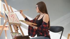 Pretty Pretty Girl artist paints on canvas painting on the easel. Studio black background. Long hair, brunette stock footage Pretty Pretty Girl artist paints on canvas painting on the easel. Studio black background. Long hair, brunette stock footage