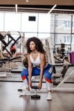 Pretty slim girl with dark curly hair dressed in a sportswear is doing back squats with heavy dumbbell in the modern gym royalty free stock photos Pretty slim girl with dark curly hair dressed in a sportswear is doing back squats with heavy dumbbell in the modern gym royalty free stock photos