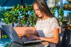 Pretty smiling blogger using laptop computer to write blogs while sitting at outdoor cafe on sunny day. royalty free stock image Pretty smiling blogger using laptop computer to write blogs while sitting at outdoor cafe on sunny day. royalty free stock image