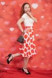 Pretty stylish pin up girl in white shirt and red polka dot vintage skirt standing on red hearts background stock photography Pretty stylish pin up girl in white shirt and red polka dot vintage skirt standing on red hearts background stock photography