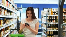 Pretty woman use phone with shopping basket in supermarket, texting sms stock video footage Pretty woman use phone with shopping basket in supermarket, texting sms stock video footage