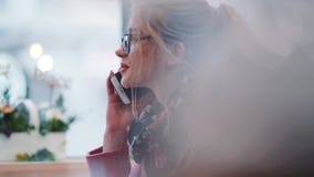 Pretty young blonde girl in a glasses sitting in the cozy café, having a phone call, smiling, nodding. Agreement stock footage Pretty young blonde girl in a glasses sitting in the cozy café, having a phone call, smiling, nodding. Agreement stock footage