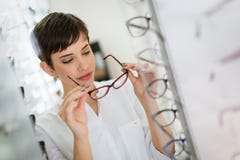Pretty young woman is choosing new glasses at optics store Royalty Free Stock Images Pretty young woman is choosing new glasses at optics store Royalty Free Stock Images