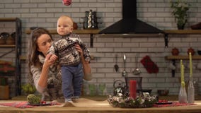 Pretty young woman and cute baby in her arms standing in modern kitchen. Happy family concept. stock footage Pretty young woman and cute baby in her arms standing in modern kitchen. Happy family concept. stock footage