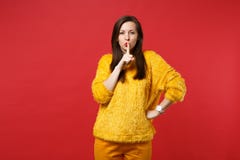 Pretty young woman in yellow fur sweater saying hush be quiet with finger on lips shhh gesture isolated on red wall stock photo Pretty young woman in yellow fur sweater saying hush be quiet with finger on lips shhh gesture isolated on red wall stock photo