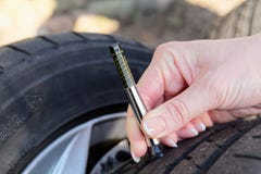 Primer de la mujer que comprueba la pisada en el neumático de coche con el indicador foto de archivo libre de regalías Primer de la mujer que comprueba la pisada en el neumático de coche con el indicador foto de archivo libre de regalías