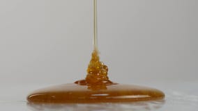 Primer del goteo de la miel Miel de colada en superficie 4K almacen de video Primer del goteo de la miel Miel de colada en superficie 4K almacen de video