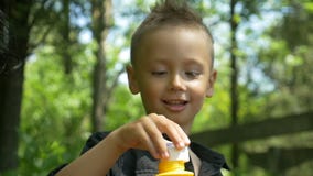 Primer del muchacho lindo feliz que sopla burbujas de jabón coloreadas en un parque soleado metrajes Primer del muchacho lindo feliz que sopla burbujas de jabón coloreadas en un parque soleado metrajes