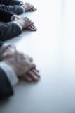 Primer en las manos dobladas de hombres de negocios en la tabla durante una reunión de negocios foto de archivo Primer en las manos dobladas de hombres de negocios en la tabla durante una reunión de negocios foto de archivo