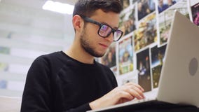 Primer tirado de hombre de negocios elegante joven en vidrios, mecanografiando en su smartphone y ordenador portátil, contra fond metrajes Primer tirado de hombre de negocios elegante joven en vidrios, mecanografiando en su smartphone y ordenador portátil, contra fond metrajes