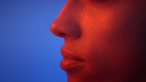 Primer tirado en el perfil de ojos y de labios del modelo de moda que es serio en luz de neón roja en fondo azul almacen de video Primer tirado en el perfil de ojos y de labios del modelo de moda que es serio en luz de neón roja en fondo azul almacen de video