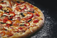 Primo piano caldo fresco della pizza deliziosa sulla tavola nera con sparso immagine stock Primo piano caldo fresco della pizza deliziosa sulla tavola nera con sparso immagine stock