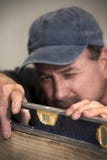 Primo piano del carpentiere maschio che esamina strumento livellato sul bordo di legno immagine stock libera da diritti Primo piano del carpentiere maschio che esamina strumento livellato sul bordo di legno immagine stock libera da diritti