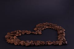 Primo piano del contorno del cuore dei chicchi di caffè su una superficie scura immagine stock libera da diritti Primo piano del contorno del cuore dei chicchi di caffè su una superficie scura immagine stock libera da diritti