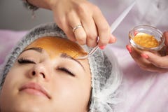 Primo piano del ritratto di bella ragazza che applica la maschera del facial dell'oro fotografia stock Primo piano del ritratto di bella ragazza che applica la maschera del facial dell'oro fotografia stock