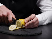 Primo piano un barista che taglia un limone Un uomo che affetta limone giallo su un fondo nero Frullato della frutta che fa conce fotografie stock Primo piano un barista che taglia un limone Un uomo che affetta limone giallo su un fondo nero Frullato della frutta che fa conce fotografie stock