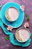 Primo-yogurt sano con le mandorle ed i fiocchi della noce di cocco in una ciotola blu su un fondo porpora decorato con i fiori di fotografia stock libera da diritti Primo-yogurt sano con le mandorle ed i fiocchi della noce di cocco in una ciotola blu su un fondo porpora decorato con i fiori di fotografia stock libera da diritti