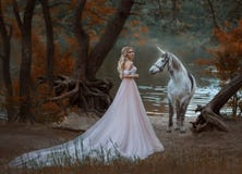 The princess met a unicorn in the forest. The blonde girl with a gentle make-up, is dressed in a long vintage dress with