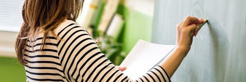 Profesor de sexo femenino joven o una fórmula de la matemáticas de la escritura del estudiante en la pizarra en sala de clase imágenes de archivo libres de regalías Profesor de sexo femenino joven o una fórmula de la matemáticas de la escritura del estudiante en la pizarra en sala de clase imágenes de archivo libres de regalías