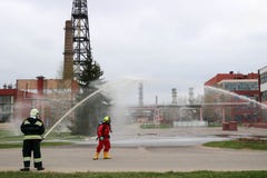 Professional firefighters in orange fire-resistant suits in white helmets with gas masks are testing fire hoses and fire guns to e royalty free stock photography Professional firefighters in orange fire-resistant suits in white helmets with gas masks are testing fire hoses and fire guns to e royalty free stock photography
