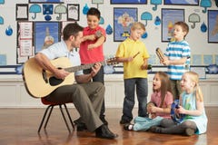 Professor masculino que joga a guitarra com pupilas foto de stock royalty free Professor masculino que joga a guitarra com pupilas foto de stock royalty free