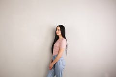 Profil av den attraktiva unga brunettkvinnan med långt hår som står av den gråa bakgrunden som bär den rosa skjortan och jeans arkivbilder Profil av den attraktiva unga brunettkvinnan med långt hår som står av den gråa bakgrunden som bär den rosa skjortan och jeans arkivbilder