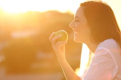 Profil d'une femme mangeant une pomme au coucher du soleil Photos stock Profil d'une femme mangeant une pomme au coucher du soleil Photos stock