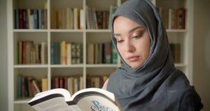 Profile portrait of muslim student in hijab reading book attentively smiles into camera at the library. stock video footage Profile portrait of muslim student in hijab reading book attentively smiles into camera at the library. stock video footage