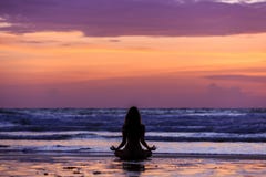 Profili la giovane donna che fa l'yoga sulla spiaggia al tramonto immagine stock libera da diritti Profili la giovane donna che fa l'yoga sulla spiaggia al tramonto immagine stock libera da diritti