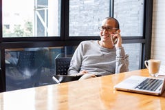 Proprietário empresarial pequeno masculino asiático alegre que fala no telefone com cliente ao sentar-se no escritório Copie o es imagem de stock Proprietário empresarial pequeno masculino asiático alegre que fala no telefone com cliente ao sentar-se no escritório Copie o es imagem de stock