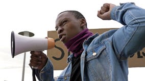 At a protest against racism dark-skinned young protester shouts angrily in megaphone.
