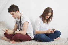 Przyjaciela wysylanie sms z telefonem komórkowym podczas gdy siedzący na kanapie zdjęcia stock Przyjaciela wysylanie sms z telefonem komórkowym podczas gdy siedzący na kanapie zdjęcia stock