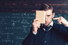 Przystojny uczeń w kostiumu zakrywa jego twarz z książką podczas gdy wskazujący przy nim z inną ręką Zbliżenie portret potomstwa zdjęcie stock Przystojny uczeń w kostiumu zakrywa jego twarz z książką podczas gdy wskazujący przy nim z inną ręką Zbliżenie portret potomstwa zdjęcie stock
