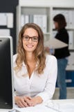 Préposée de bureau s'asseyante dans blanc regardant l'appareil-photo image stock Préposée de bureau s'asseyante dans blanc regardant l'appareil-photo image stock