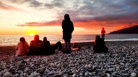 Puesta del sol de observación del grupo de personas en la playa foto de archivo Puesta del sol de observación del grupo de personas en la playa foto de archivo