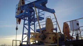 Pumpjack on an oil well in winter forest in daytime, extraction of petroleum in northern countries
