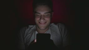 Punto di vista dell'angolo alto di un giovane attraente che passa in rassegna media sociali su uno Smart Phone a letto video d archivio Punto di vista dell'angolo alto di un giovane attraente che passa in rassegna media sociali su uno Smart Phone a letto video d archivio