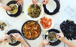 Punto di vista superiore della famiglia che mangia paella e frutti di mare intorno ad una tavola bianca dall'alto angolo di vista fotografia stock Punto di vista superiore della famiglia che mangia paella e frutti di mare intorno ad una tavola bianca dall'alto angolo di vista fotografia stock