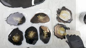 Putting black epoxy resin with pieces of gold leaf on the multiple mold resin coaster. Top View and close up. White marble