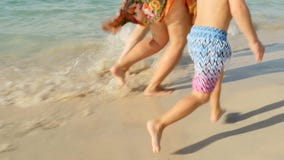 På solnedgången behandla som ett barn den lyckliga familjmamman, farsa och rinnande barfota på våt sand havsbränning, närbild av lager videofilmer På solnedgången behandla som ett barn den lyckliga familjmamman, farsa och rinnande barfota på våt sand havsbränning, närbild av lager videofilmer