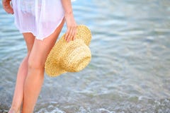 Pés da mulher e um chapéu de palha à disposição na praia na água do mar fotos de stock Pés da mulher e um chapéu de palha à disposição na praia na água do mar fotos de stock