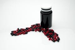 Píldoras antibióticos rojas, negras de la cápsula y botella plástica marrón aisladas en el fondo blanco con el espacio de la copi Fotografía de archivo Píldoras antibióticos rojas, negras de la cápsula y botella plástica marrón aisladas en el fondo blanco con el espacio de la copi Fotografía de archivo