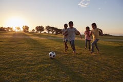 Quatre enfants chassant une boule pendant un jeu dans un domaine photo stock Quatre enfants chassant une boule pendant un jeu dans un domaine photo stock