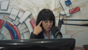 Radio DJ en el estudio de la difusión La muchacha pone un finger a su cabeza, representando cansancio almacen de metraje de vídeo Radio DJ en el estudio de la difusión La muchacha pone un finger a su cabeza, representando cansancio almacen de metraje de vídeo