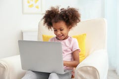 Ragazza afroamericana piccola con il computer portatile che si siede in poltrona fotografia stock libera da diritti Ragazza afroamericana piccola con il computer portatile che si siede in poltrona fotografia stock libera da diritti