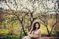 Ragazza castana riccia che sta negli alberi sboccianti fotografia stock Ragazza castana riccia che sta negli alberi sboccianti fotografia stock