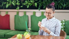 Ragazza casuale sorridente sulla dieta che mangia yogurt fresco che si siede sulla tavola nel colpo di medium del caffè stock footage Ragazza casuale sorridente sulla dieta che mangia yogurt fresco che si siede sulla tavola nel colpo di medium del caffè stock footage