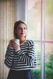 Ragazza con il soggiorno della tazza di caffè vicino alla finestra fotografia stock libera da diritti Ragazza con il soggiorno della tazza di caffè vicino alla finestra fotografia stock libera da diritti