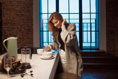 Ragazza incantante nella cucina alla mattina Parlando sul telefono ed avere giovane donna della prima colazione A con la tazza in fotografia stock libera da diritti Ragazza incantante nella cucina alla mattina Parlando sul telefono ed avere giovane donna della prima colazione A con la tazza in fotografia stock libera da diritti
