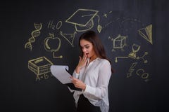 Ragazza sorpresa, guardante in una cartella con i documenti, stanti accanto ad una lavagna fotografia stock Ragazza sorpresa, guardante in una cartella con i documenti, stanti accanto ad una lavagna fotografia stock